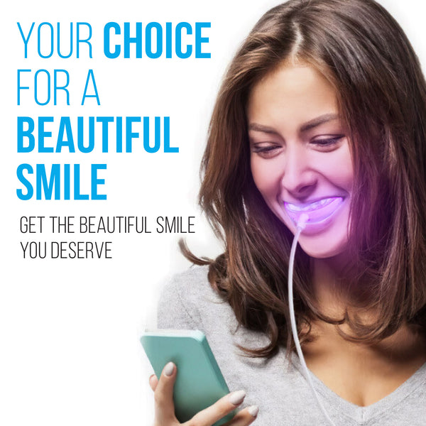 Woman using red and blue LED gum stimulator light while smiling and holding phone.